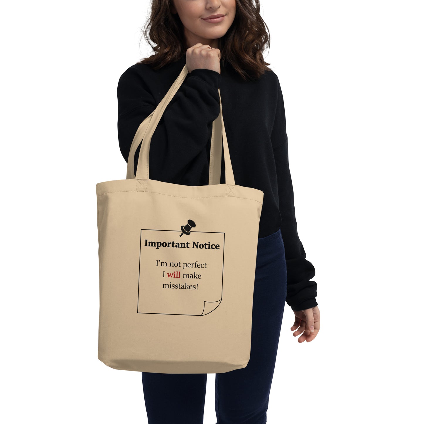 A woman carrying a small oyster colour organic cotton twill tote, showcasing a printed black outlined square note and a black pushpin at the top centre. The note displays the slogan: "Important notice: I’m not perfect, I will make mistakes" in black, with will in bold red for emphasis.