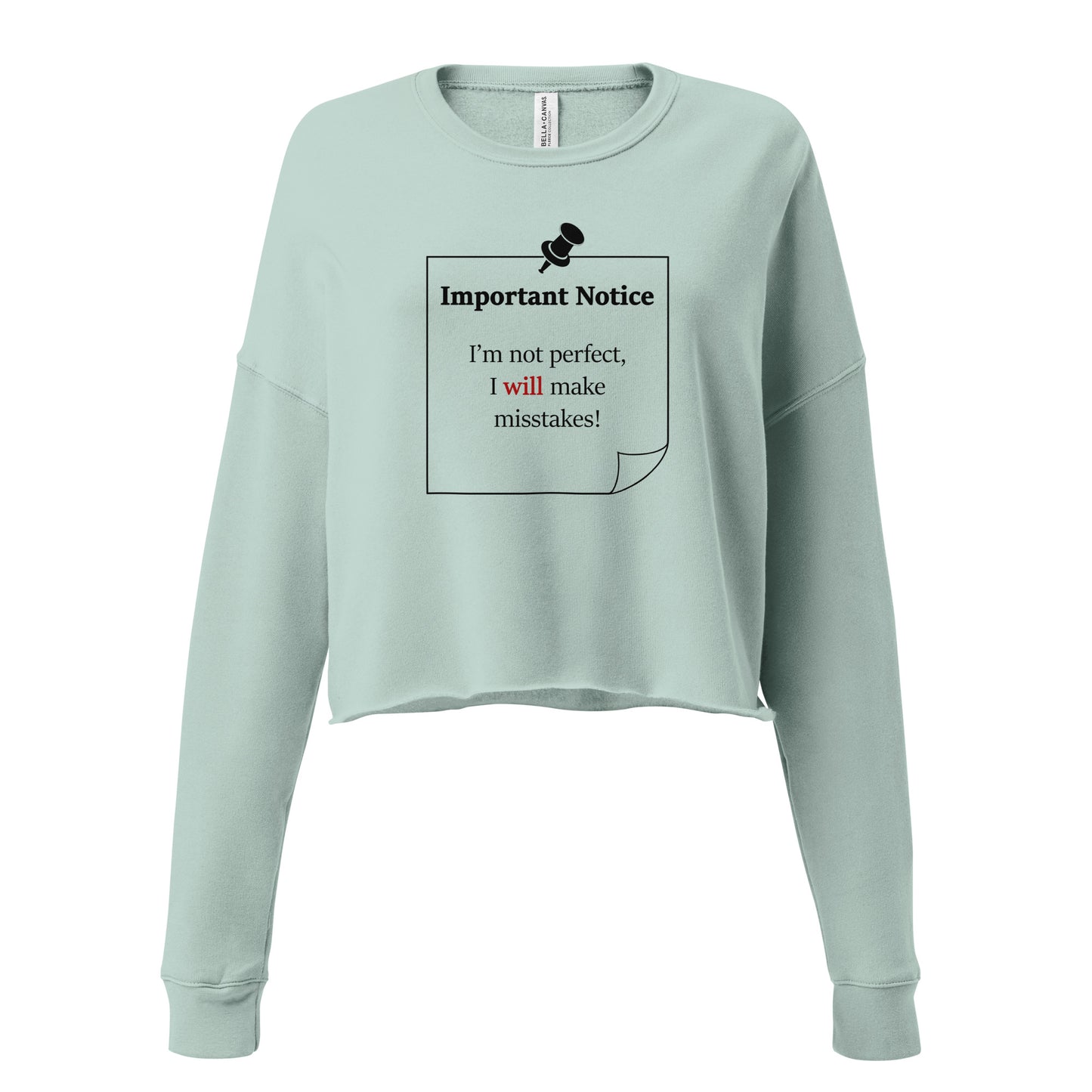 A woman’s cropped fleece dusty blue sweatshirt jumper featuring a printed black outlined square note and a black pushpin at the top centre. The note displays the slogan: "Important notice: I’m not perfect, I will make mistakes" in black, with the word will highlighted in bold red for emphasis.