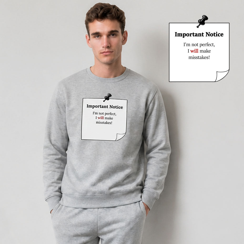 A man in grey track bottoms wearing a grey classic jumper, featuring a printed black-outlined square note with a black pushpin. The note displays the slogan: 'Important Notice: I’m not perfect, I will make mistakes,' with 'will' in bold red for emphasis.
