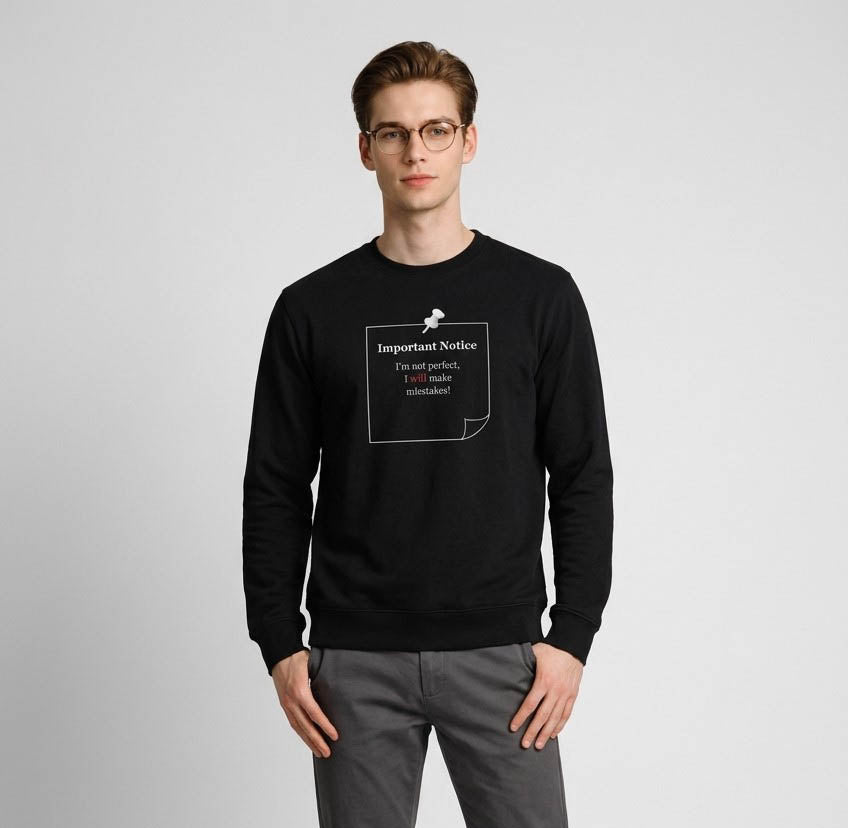 A man in cargo's wearing a black classic jumper, featuring a printed black-outlined square note with a black pushpin. The note displays the slogan: 'Important Notice: I’m not perfect, I will make mistakes,' with 'will' in bold red for emphasis.