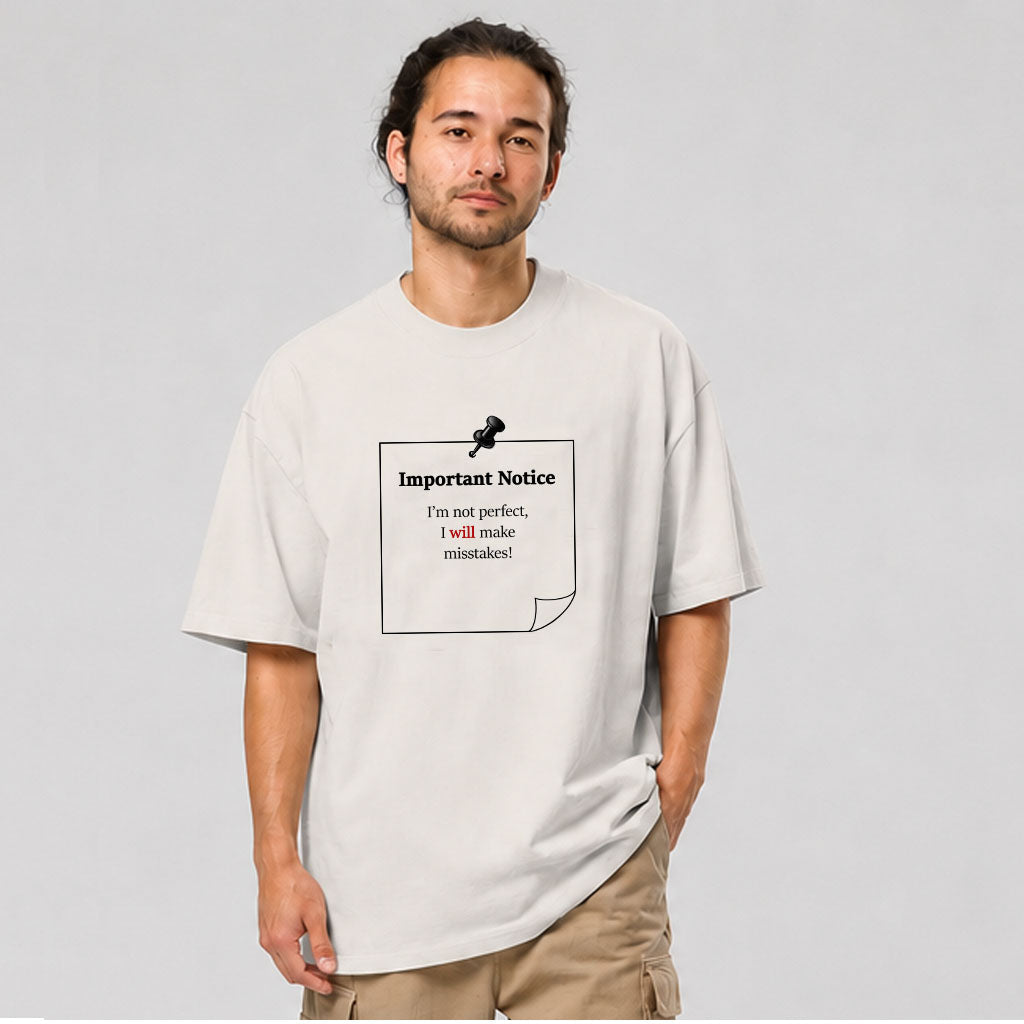 A man in shorts wearing a khaki oversized t-shirt and a woman in shorts wearing a eucalyptus oversized t-shirt. Both featuring a slogan: 'Important notice: I’m not perfect, I will make mistakes.