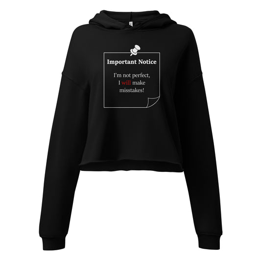 A woman’s black hoodie cropped sweatshirt jumper featuring a printed white-outlined square note and a white pushpin at the top centre. The note displays the slogan: "Important notice: I’m not perfect, I will make mistakes" in black, with the word will highlighted in bold red for emphasis.