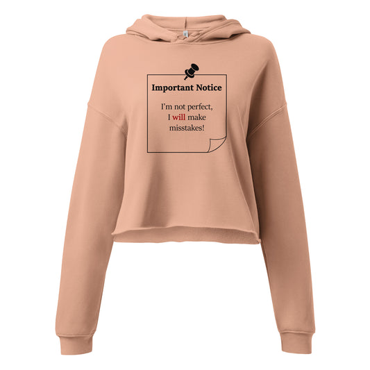 A woman’s peach hoodie cropped sweatshirt jumper featuring a printed black outlined square note and a black pushpin at the top centre. The note displays the slogan: "Important notice: I’m not perfect, I will make mistakes" in black, with the word will highlighted in bold red for emphasis.